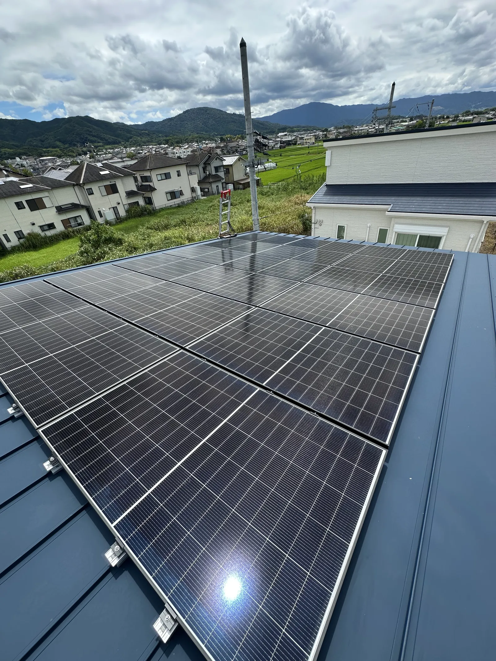 長期優良住宅の片流れ屋根に太陽光パネルを設置している実際の様子。手前にパネル面が敷き詰まり、奥に電柱と山並みが見える