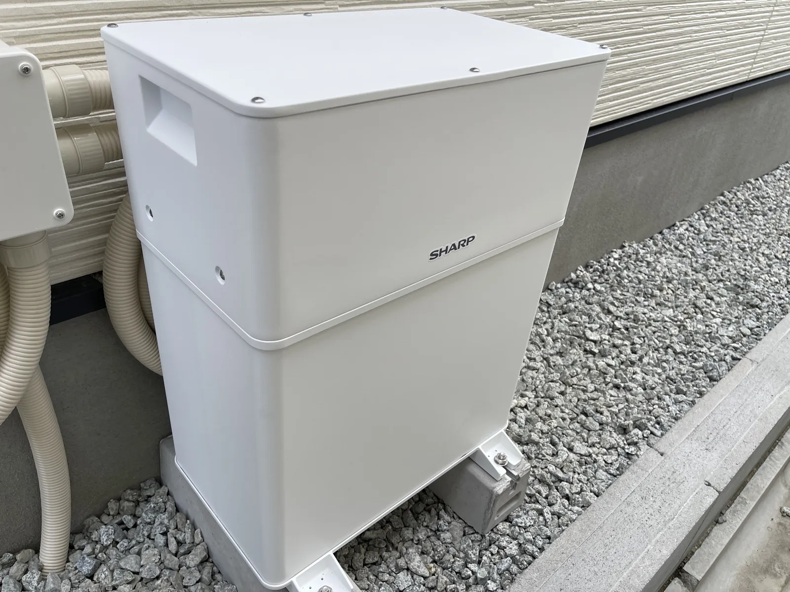 新築入居後に専門業者へ依頼して後付けされた白い蓄電池ユニットの実物。外壁沿いの犬走りに基礎ブロックで据え付けられている様子