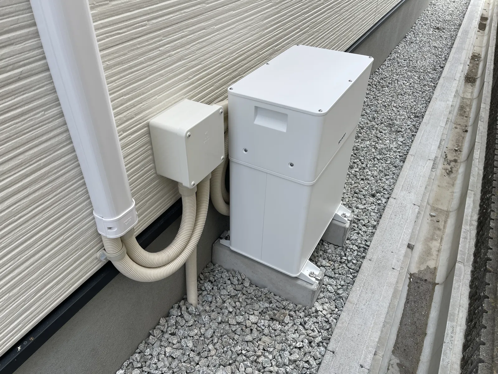 犬走りの砕石の上に置かれたブロック2本の上に据え付けられた白い屋外蓄電池ユニット
